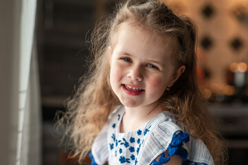 A cute little girl with long curly hair looks out the window. Portrait. Close-up