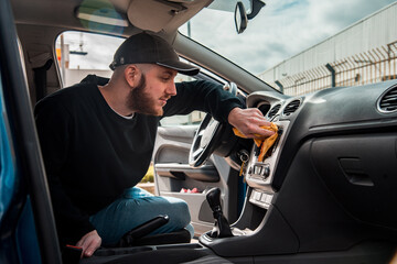 Hombre joven con gorra limpiando la pantalla del salpicadero del interior de su coche con un paño. Quitar el polvo del salpicadero del coche con un trapo