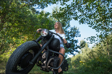 Fototapeta na wymiar Biker girl on a motorcycle on a forest road.