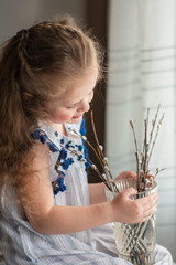 Cute little girl with long curly hair sits by the window with pussy willow branches