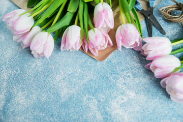 pink spring tulips on a blue textured background, next to twine rope and scissors, preparing bouquets for the holiday