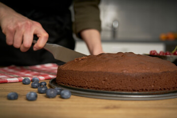 Woman with a passion for cooking cuts a slice of handmade chocolate cake in her home kitchen.