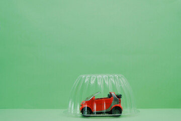 Red small car toy protected under a plastic dome. Mint background. Car insurance concept. Copy space.