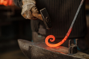 The blacksmith hits the red-hot workpiece in the forge with a hammer and glowing sparks fly in all...