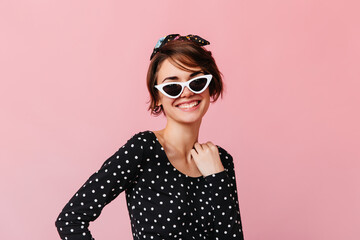 Enthusiastic short-haired girl posing in sunglasses. Studio shot of blissful young woman isolated on pink background.
