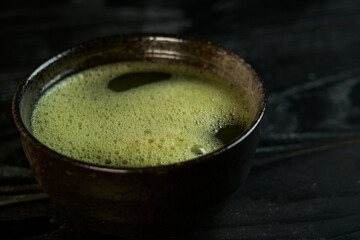 Japanese organic matcha green tea in bowl with chashaku spoon and chasen bamboo whisk on black wooden background. Healthy product from the nature typical of the Japanese tradition. Tea ceremony.