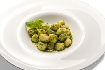 Gnocchi al pesto from Genoa, traditional Italian recipe made of fresh basil, olive oil, pine nuts. In white dish isolated on white