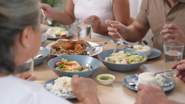 Asian family having dinner together at home. Smiling adult couple with senior parents enjoy eating and sharing thai food on dining table. Happy family spending time together on weekend vacation.