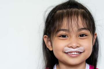 Close up fun portrait of cute Asian girl showing white milk mustache.Isolated against light...