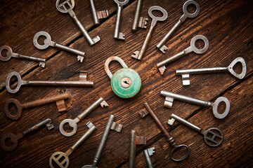 Vintage rusty padlock surrounded by group of old keys on a weathered wooden background. Internet security and data protection concept, blockchain and cybersecurity