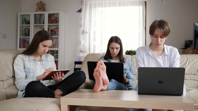Distance school education at home three triplet sisters teenager girls use laptop computers and tablet for learning preparing lessons making tasks together