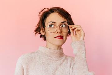 Pensive good-looking woman touching glasses. Studio shot of beautiful short-haired girl isolated on pink background.