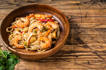 Udon stir-fry noodles with shrimp prawns in a wooden bowl. wooden background. Top view. Copy space