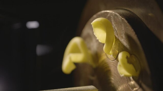 Close-up.Professional production of pasta(Trottole). Pasta dough coming out of the extruder is automatically cut. Steam created by the heat in the extruder are visible. UHD, 4K