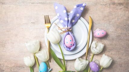 Easter holiday table setting with bunny  from egg on white plate and tulips flowers.  Gray concrete...