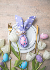 Easter holiday table setting with bunny  from egg on white plate and tulips flowers.  Gray concrete table, top view with copy space for text. Happy Easter background