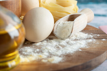 Tagliatelle with oil, egg and bowl of flour on wooden board