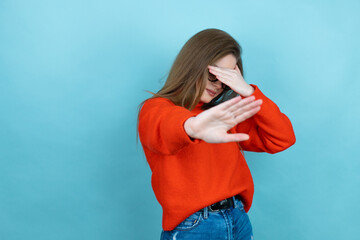 Pretty woman with long hair wearing a casual sweater and glasses over blue background covering eyes with hands and doing stop gesture with sad and fear expression. Embarrassed and negative concept.