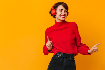 Emotional girl in red sweater dancing with smile. Studio shot of inspired woman in headphones.