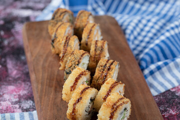 Hot fried sushi rolls with mixed ingredients and crispy cover on a wooden board