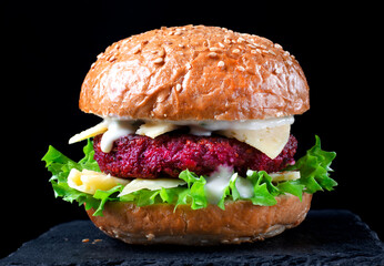 Beet burger with lettuce, cheese and yogurt sauce against the black background