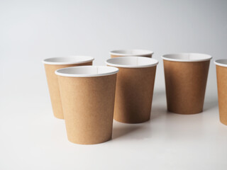 Several paper disposable brown cups are randomly placed on a white background