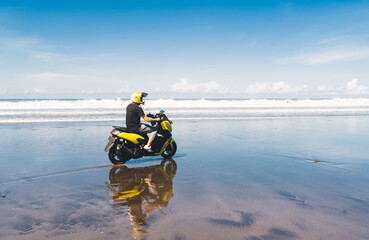 Unrecognizable man in helmet riding motorbike on sandy sea coastline