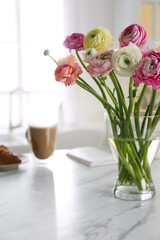 Beautiful fresh ranunculus flowers near cup of coffee and book on table in kitchen