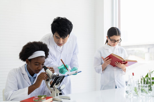 Asian teacher and diverse student doing tests of plants in classroom. Group of diversity scientists learning science and doing analysis for germs and bacteria with microscope in the laboratory