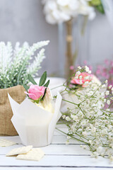 Several cupcakes and muffins with white butter cream and a lively pink rose on a white wooden table. Valentine's day or Mother's Day gift. Fresh flowers are on the table nearby. Rustic style.