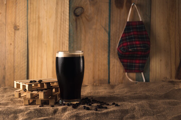 Black beer on a little pallet, with coffee in a wood and industrial background. Mask hanging on the...