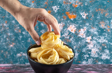 Male hand holding tagliatelle nest on colorful background