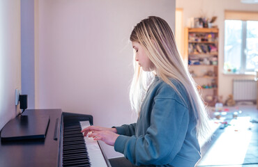 Blonde teenage girl playing electric piano at home