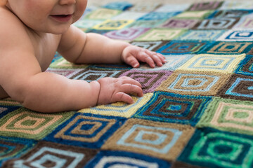 Young baby doing tummy time on handmade knitted blanket; learning to crawl