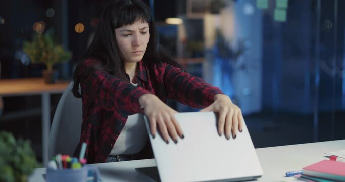 Tired sleepy caucasian young woman closing laptop device fisnihing her work leaning down in chair. Sleepy employee. Exhaustion from work.