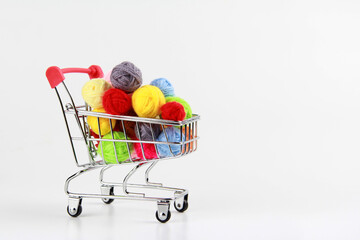 Lots of all colors of yarn balls for knitting or crocheting on a white background, in a small shopping cart.Top view.Flatlay.Copyspace.