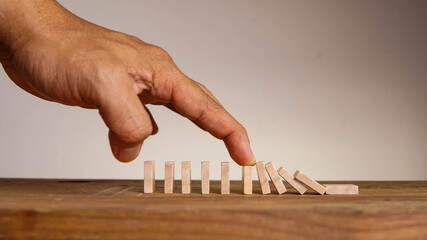 Man hand preventing wooden dominos to collapse in a conceptual image.