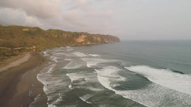 sandy beach parangtritis near ocean with big waves, people in tropical resort at sunset. Yogyakarta, Indonesia. aerial view seascape, ocean and beautiful beach. Travel concept. Indonesia, java