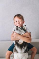 Happy little boy hugging husky dog at home
