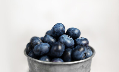 Fresh blueberries in a small metal bucket surrounded with some berries on a checked napkin. Side view. Rustic.