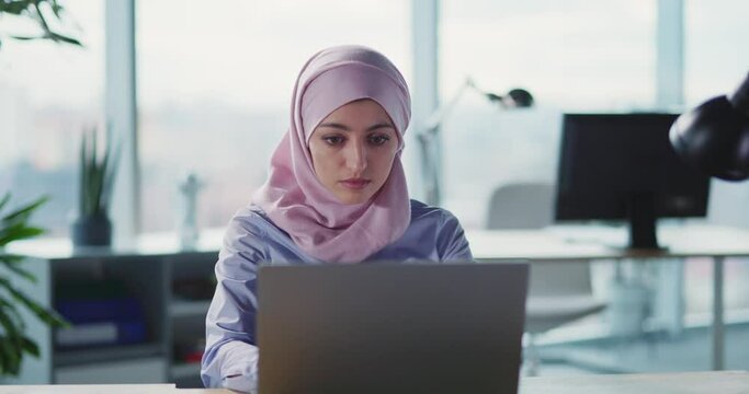 Young beautiufl arabic woman in business office wearing hijab working on laptop typing keyboard. Corporate girl. Traditional Muslim.