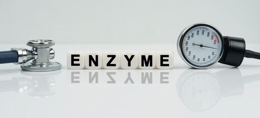 On a reflective white surface lies a stethoscope and cubes with the inscription - ENZYME