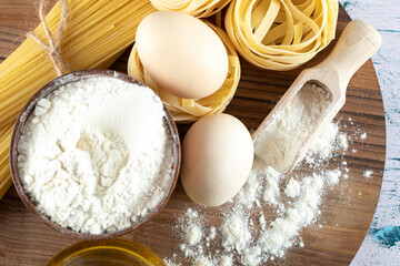 Two kinds raw pasta with oil, egg and bowl of flour on wooden board