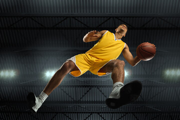 Young professional basketball player in action, motion isolated on black background, look from the...
