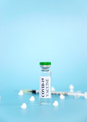Coronavirus COVID-19 vaccine in glass vial with white heart shape tablets and syringe on blue background. World prevention of pandemic. Panacea against Corona Virus.