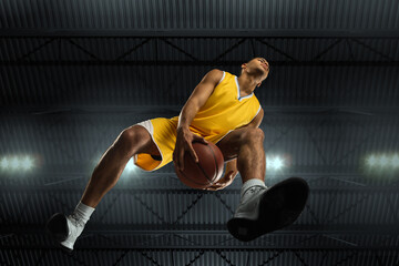 Young professional basketball player in action, motion isolated on black background, look from the...