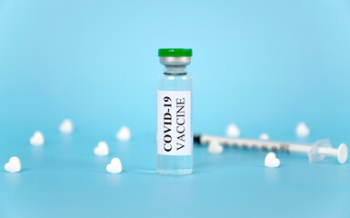 Coronavirus COVID-19 vaccine in glass vial with white heart shape tablets and syringe on blue background. World prevention of pandemic. Panacea against Corona Virus.
