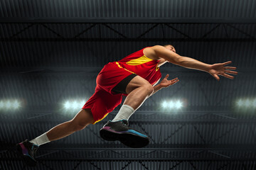 Young professional basketball player in action, motion isolated on black background, look from the...