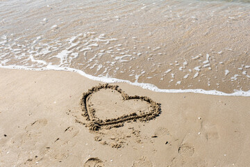 A drawing of a heart on a yellow sand at a beautiful seascape background. Horizontal composition.