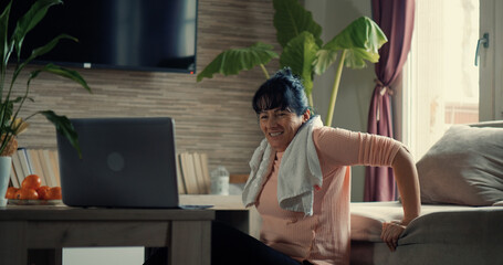 Home Workout of adult woman doing triceps dips on sofa watching fitness video tutorial online on...